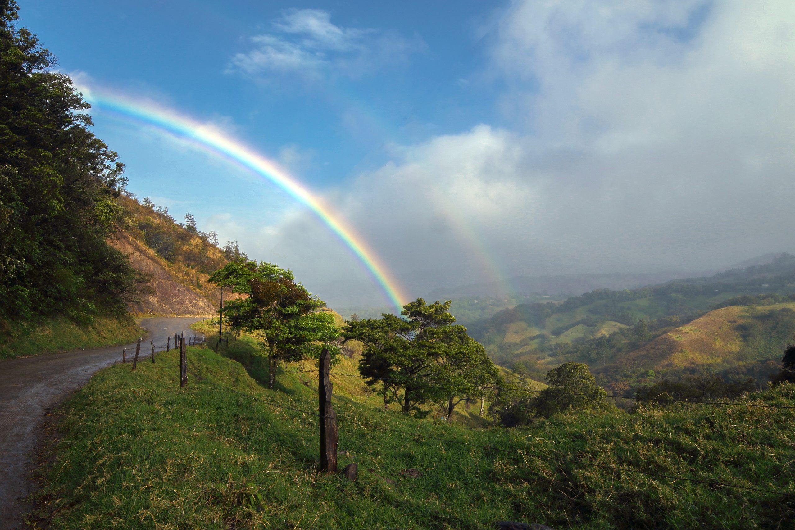 Scenic rainbow over lush mountains and country road in Costa Rica.
