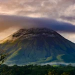 Arenal Volcano in Costa Rica during sunset, with dramatic clouds and lush green landscape.