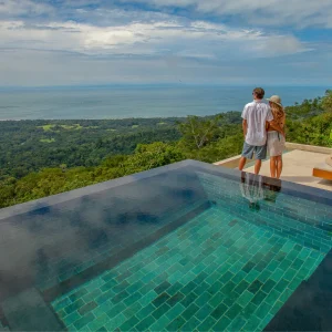 Couple standing near an infinity pool with a scenic view of Costa Rica's Pacific coastline and lush jungle.