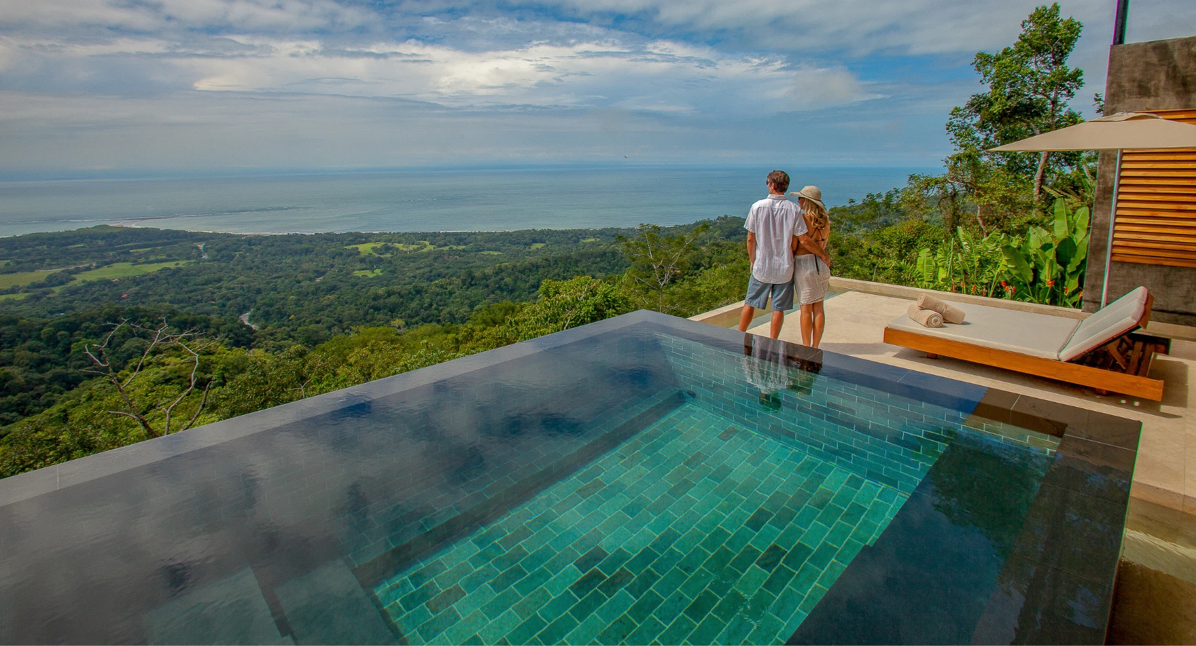 Couple standing near an infinity pool with a scenic view of Costa Rica's Pacific coastline and lush jungle.