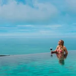Woman relaxing in an infinity pool with wine, enjoying panoramic views of the Pacific Coast in Costa Rica.