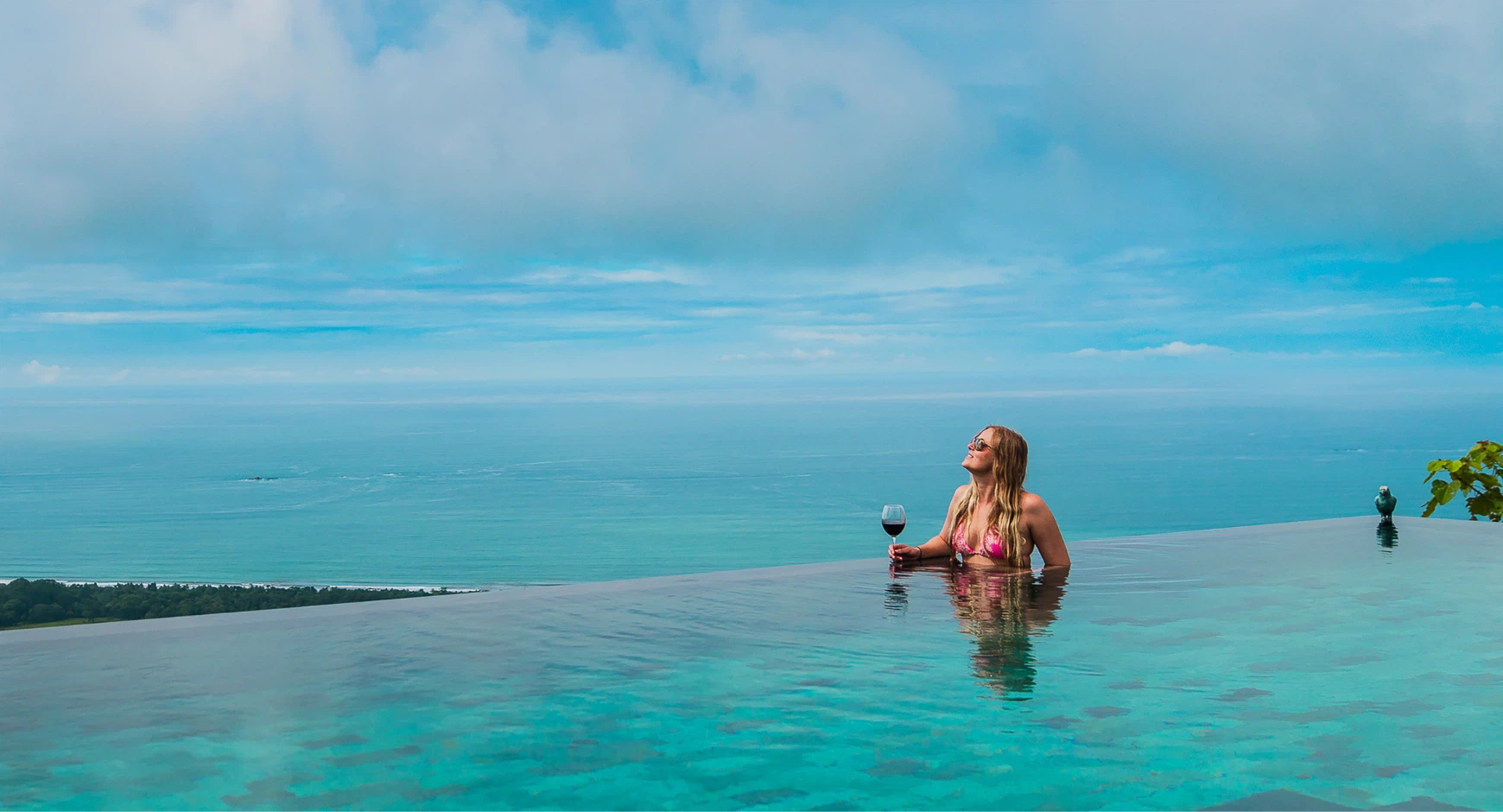 Woman relaxing in an infinity pool with wine, enjoying panoramic views of the Pacific Coast in Costa Rica.