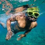 Man snorkeling in clear tropical water in Costa Rica, wearing bright yellow goggles.