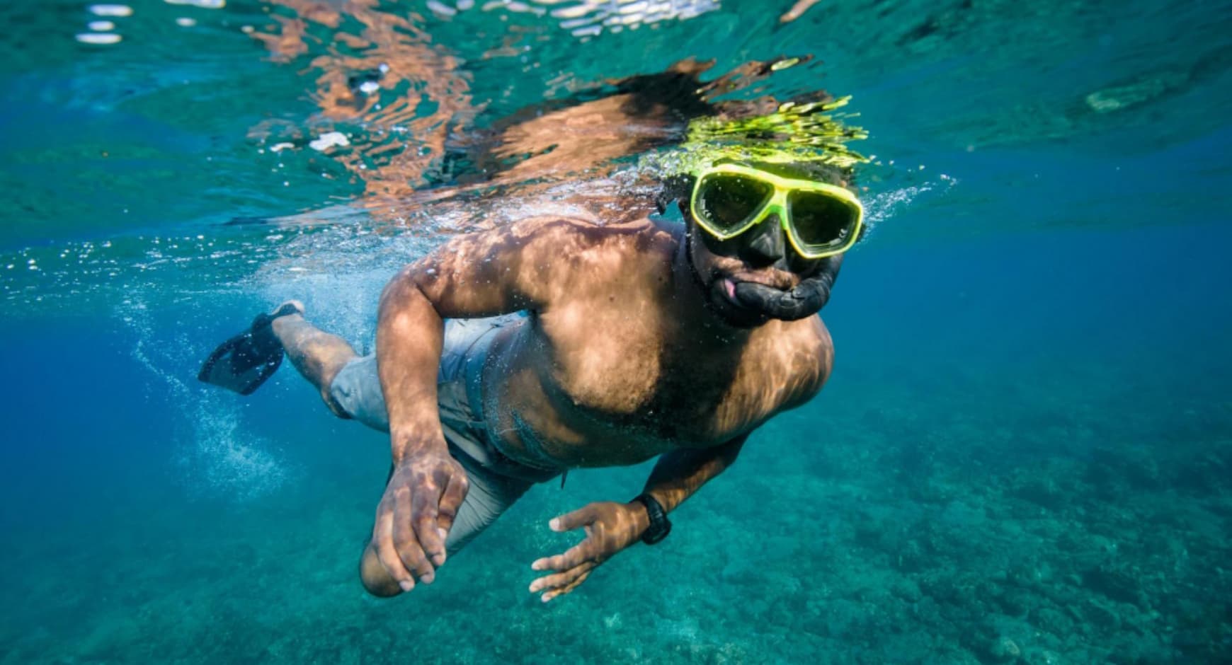 Man snorkeling in clear tropical water in Costa Rica, wearing bright yellow goggles.