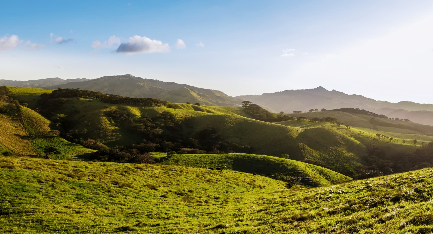 Panoramic view of green rolling hills in the highlands of Costa Rica under a blue sky.