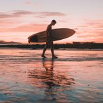 Silhouette of a surfer walking along the beach at sunset in Costa Rica.