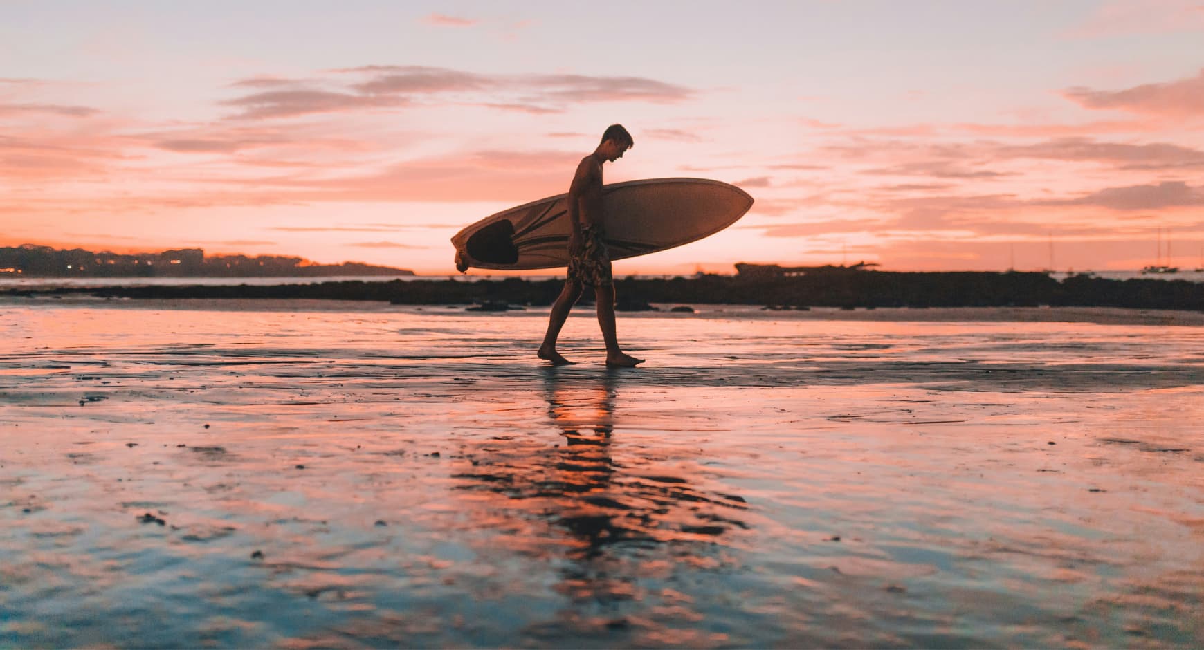 Silhouette of a surfer walking along the beach at sunset in Costa Rica.