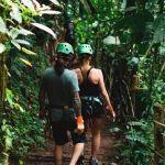 Couple walking through the jungle with helmets and harnesses, starting a canopy adventure in Costa Rica’s lush rainforest.