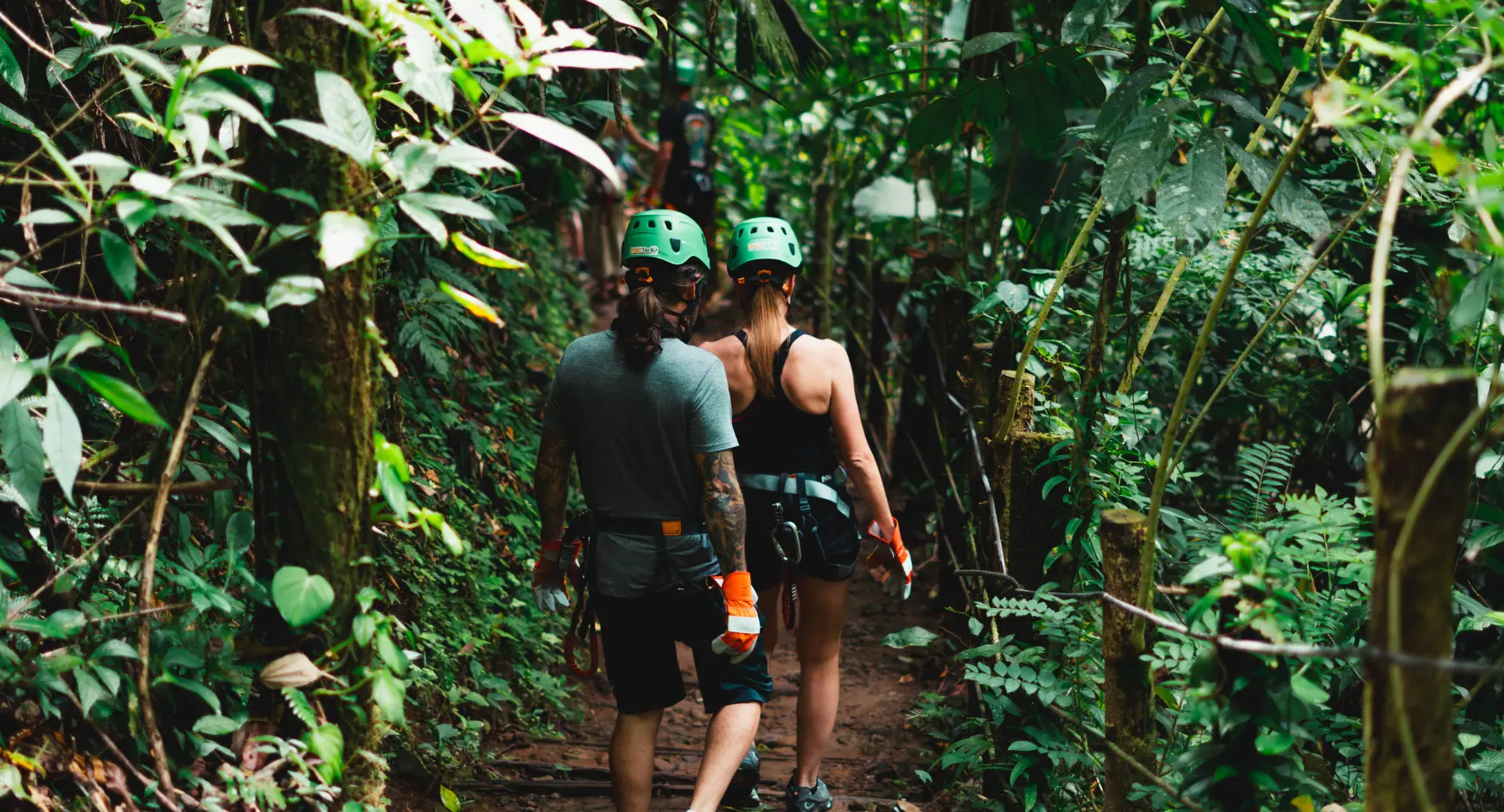 Couple walking through the jungle with helmets and harnesses, starting a canopy adventure in Costa Rica’s lush rainforest.