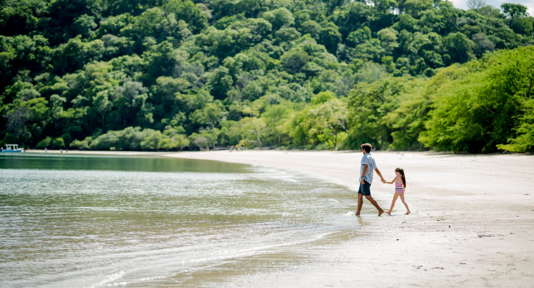 Dad and daughter walking along a peaceful beach in Papagayo, Costa Rica, surrounded by lush green jungle.