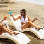 Two women enjoying colorful tropical cocktails while lounging on a Pacific Coast beach in Costa Rica.