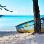 A small colorful boat tied to a tree on a peaceful Pacific Coast beach in Costa Rica, with turquoise waters in the background.