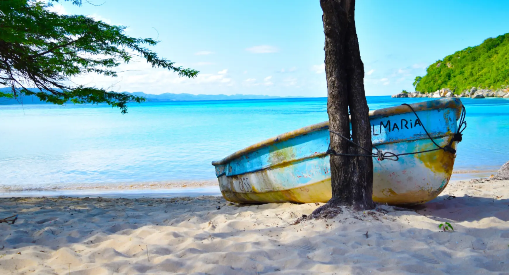 A small colorful boat tied to a tree on a peaceful Pacific Coast beach in Costa Rica, with turquoise waters in the background.