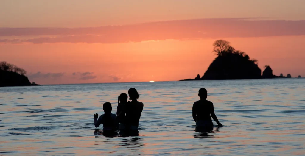 People swimming at the beach in Costa Rica during a colorful sunset