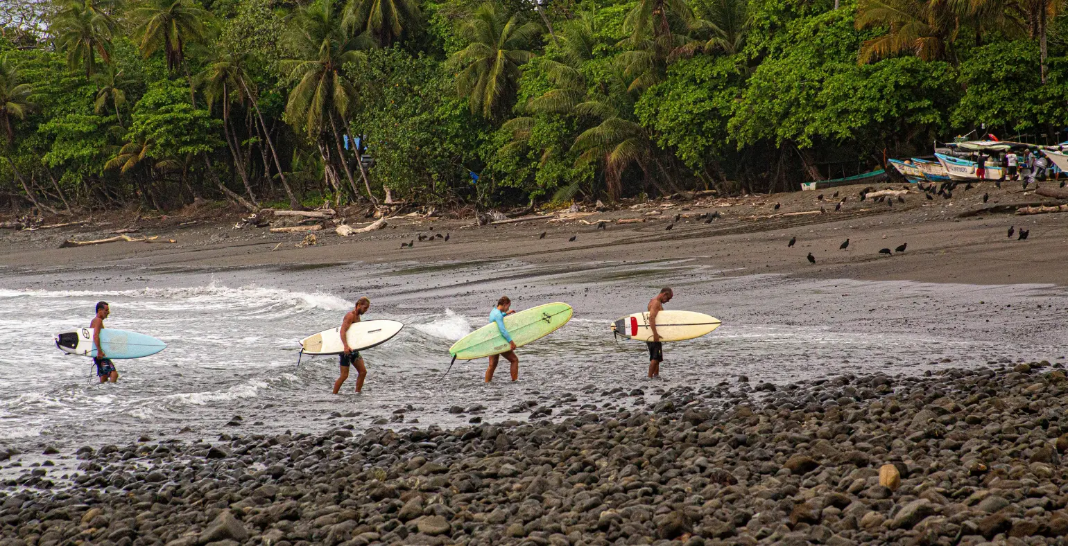 Surfers walking along a rocky beach in Costa Rica preparing to enter the water